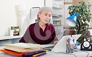 Busy focused aged female entrepreneur working with papers and laptop