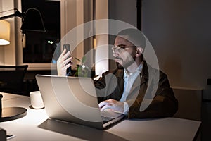 Busy front end developer or qa engineer testing app on smartphone work overtime in coworking space