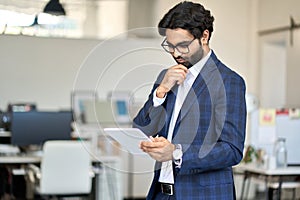 Busy indian young business man executive wearing suit using digital tablet.