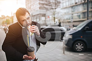 Busy man is in a hurry, he does not have time, he is going to eat snack on the go. Worker eating, drinking coffee