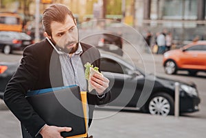 Busy man is in a hurry, he does not have time, he is going to eat snack on the go. Worker eating, drinking coffee