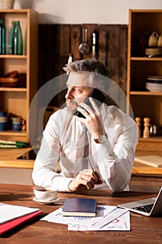 Busy man talking by phone in kitchen