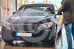 Busy man is washing his own car at car washing station.