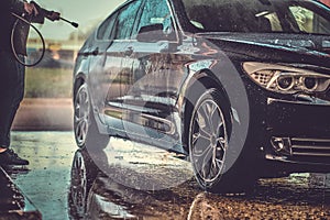 Busy man is washing his own car at car washing station.