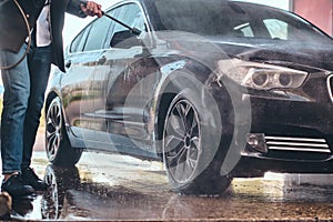 Busy man is washing his own car at car washing station.