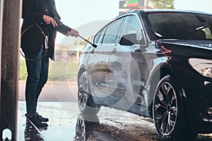 Busy man is washing his own car at car washing station.