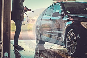 Busy man is washing his own car at car washing station.