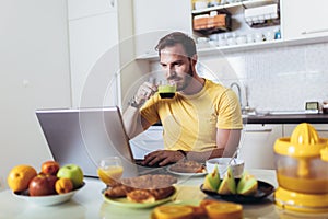 Man working at home, using laptop while having breakfast