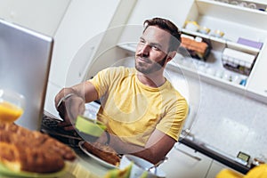 Man working at home, using laptop while having breakfast