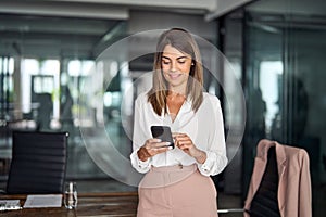 Busy mature business woman using cellphone standing in office.