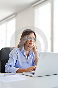 Busy mature business woman using laptop computer working in office. Vertical.