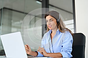 Busy mature woman call center support agent working using laptop in office.