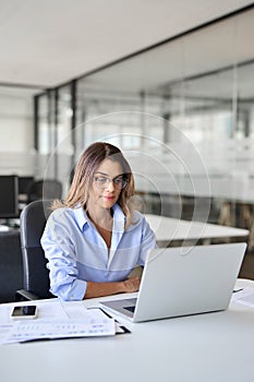 Busy middle aged business woman using laptop working in office. Vertical.
