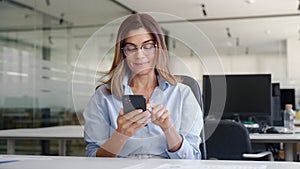 Busy middle aged business woman using mobile phone working in office.