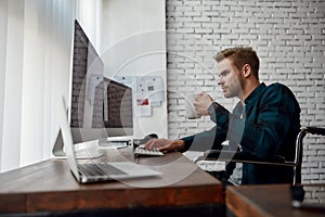 Busy morning. Side view of young web developer in a wheelchair writing program code on multiple computer screens and