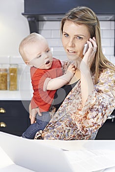 Busy Mother With Baby Coping With Stressful Day At Home