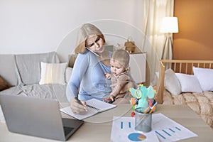 Busy mother with baby on her lap having phone conversation