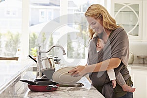 Busy Mother With Baby In Sling Multitasking At Home