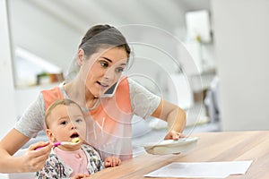 Busy mother feeding baby and talking on the phone