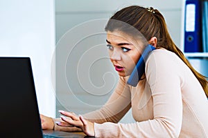 Busy office girl talking on phone and typing on laptop