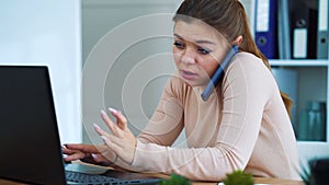 Busy office girl talking on phone and typing on laptop