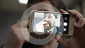 Busy office worker cranks and looking into phone camera. funy businessman picks finger in nose, strokes his beard