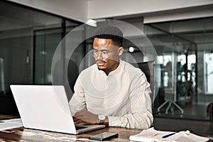 Busy professional male African company employee using laptop working in office.