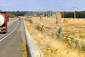 A busy road winds through harvested fields and green gardens on an autumn day