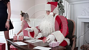Busy Santa answering chidlren`s letters while Santa`s little helpers bringing more presents