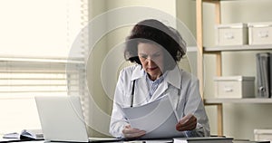 Busy senior female physician work with medical documentation using laptop