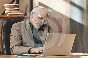 Busy senior man with phone at laptop. Multitasking at work