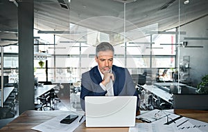 Busy serious business man ceo looking at laptop thinking in modern office.