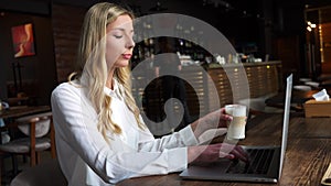 Busy smart young professional business woman using laptop computer drinking coffee during lunch in cafe. Lady