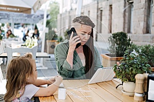 Busy Successful Mother and Business Owner with cell phone and tablet having breakfast with her little baby daughter in