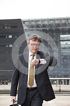 Busy well dressed businessman with briefcase in hand walking fast and checking time on his wristwatch