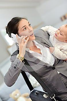 Busy woman talking on the phone and carrying her baby photo