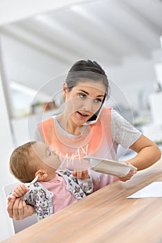 Busy woman talking on the phone and feeding her baby