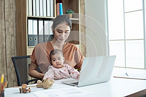 Busy woman trying to work while babysitting newborn baby daughte.  Young beautiful Asian mother holding little baby on lap while