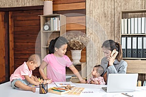 Busy woman trying to work while babysitting three kids.  Young Asian mother on a call with three children playing around her .