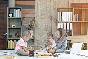 Busy woman trying to work while babysitting two kids.  Young Asian mother talking and playing with two children playing around her