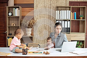 Busy woman trying to work while babysitting two kids.  Young Asian mother talking and playing with two children playing around her