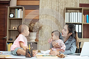 Busy woman trying to work while babysitting two kids.  Young Asian mother talking and playing with two children playing around her