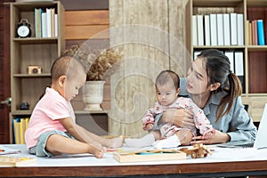 Busy woman trying to work while babysitting two kids.  Young Asian mother talking and playing with two children playing around her