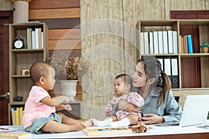 Busy woman trying to work while babysitting two kids.  Young Asian mother talking and playing with two children playing around her