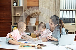 Busy woman trying to work while babysitting two kids.  Young Asian mother talking and playing with two children playing around her