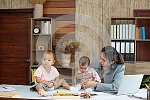 Busy woman trying to work while babysitting two kids.  Young Asian mother talking and playing with two children playing around her