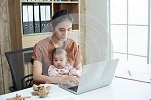 Busy woman trying to work while babysitting newborn baby daughte.  Young beautiful Asian mother holding little baby on lap while photo