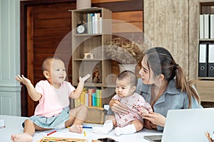 Busy woman trying to work while babysitting two kids.  Young Asian mother talking and playing with two children playing around her