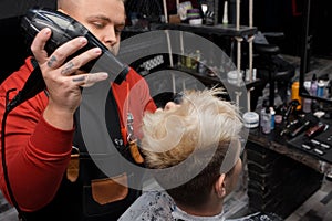 Busy work a man, a barbershop worker, a professional, blow-drying his hair to a client during the cutting process