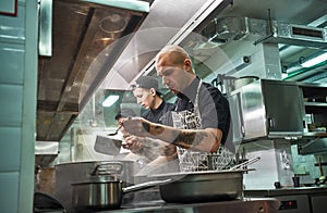 Busy working day. Professional team of restaurant chef and his two young assistants cooking at modern kitchen